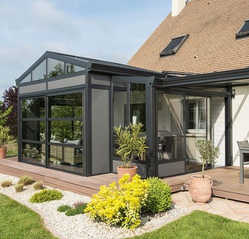 Véranda aluminium Installux gamme Luciole attenante à une maison contemporaine avec terrasse en bois et jardin paysager